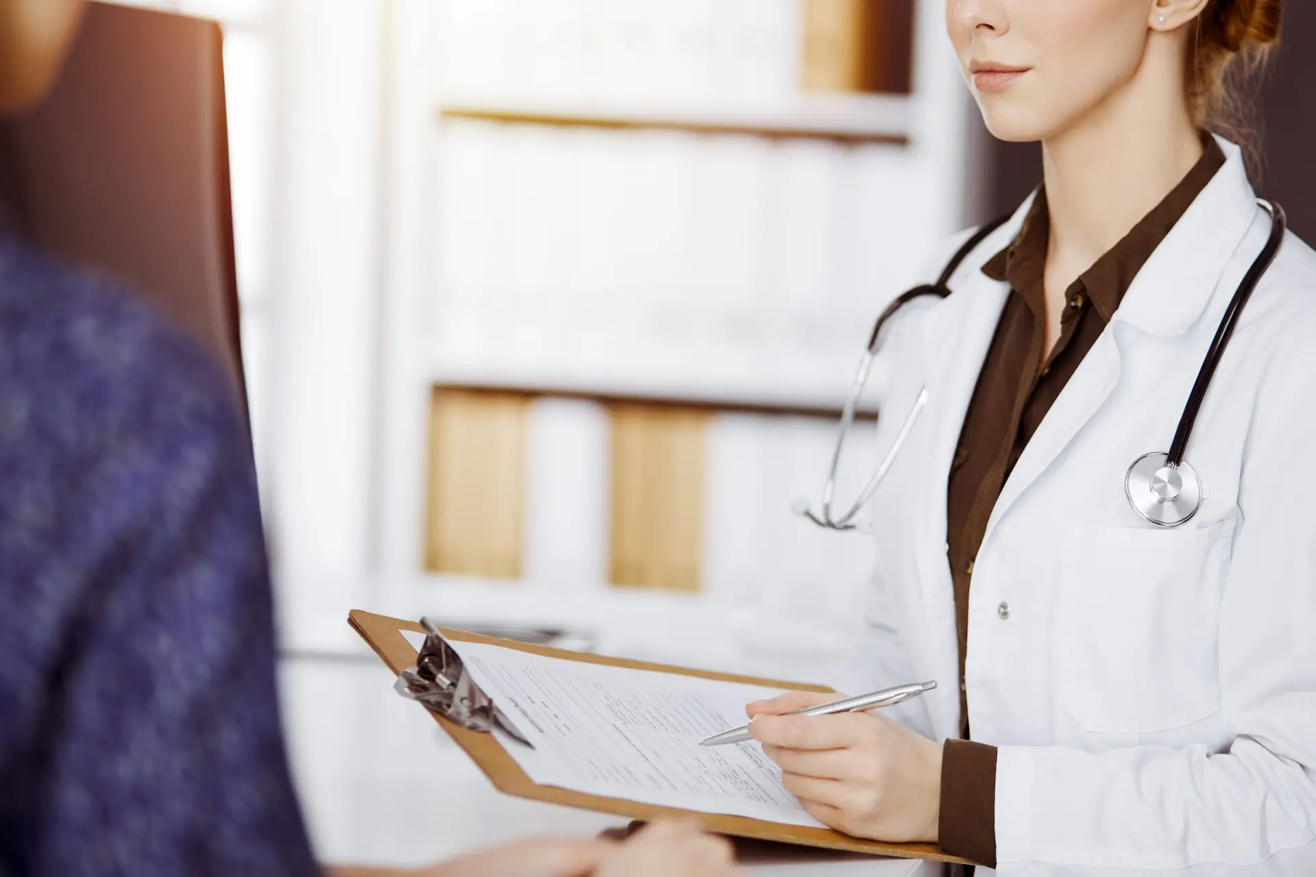 Medico in camice bianco ascolta paziente, dimostrando empatia, professionalità e fiducia in clinica.